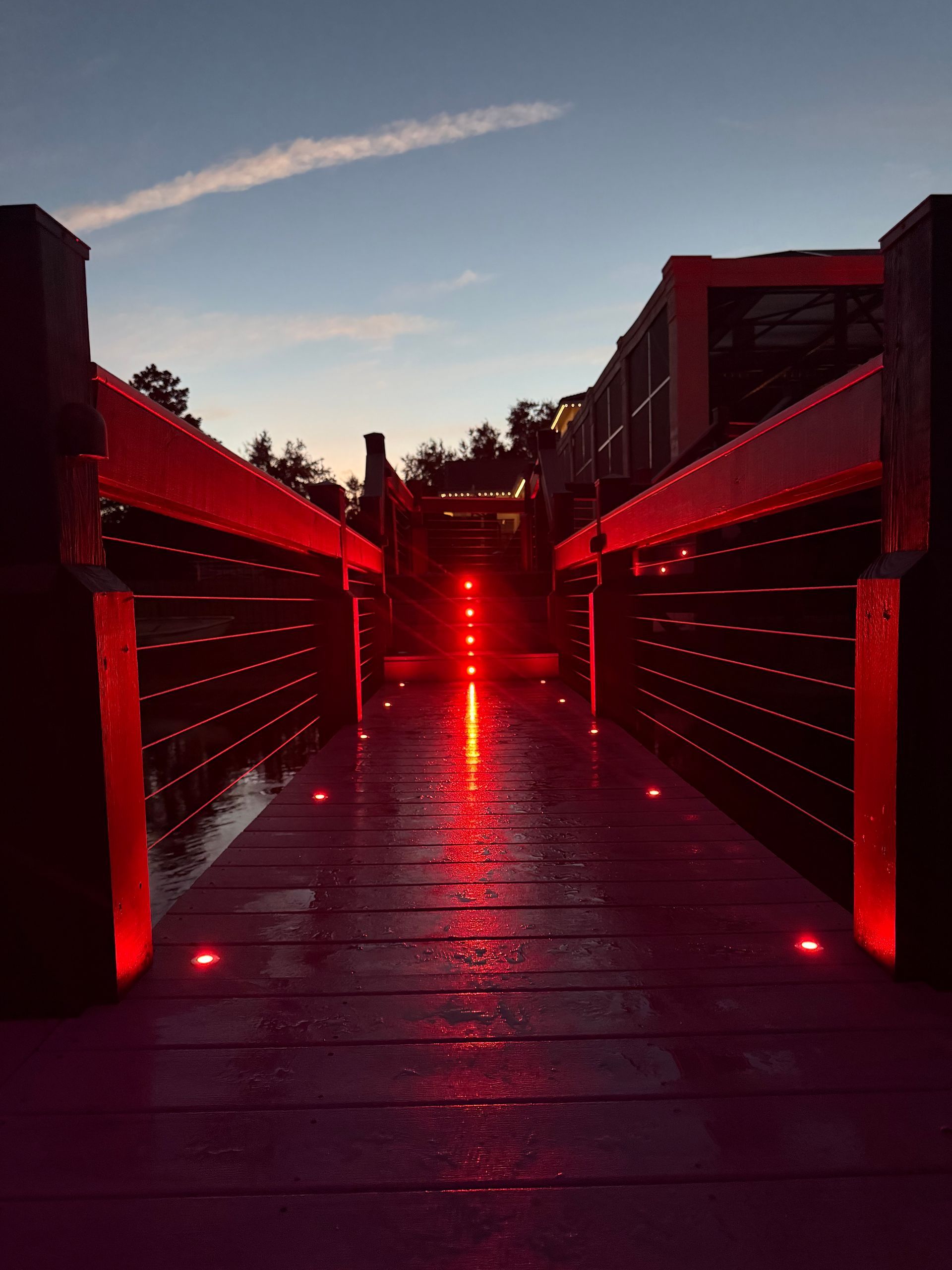 Wooden bridge with red lights at dusk. Reflections on wet planks.