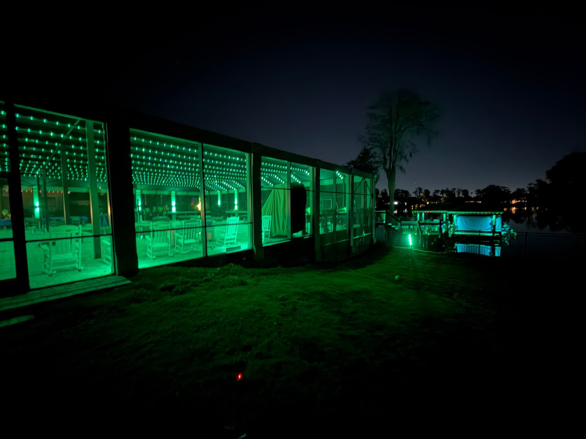 A long building with green lights at night. A smaller structure with green lights is in the distance.