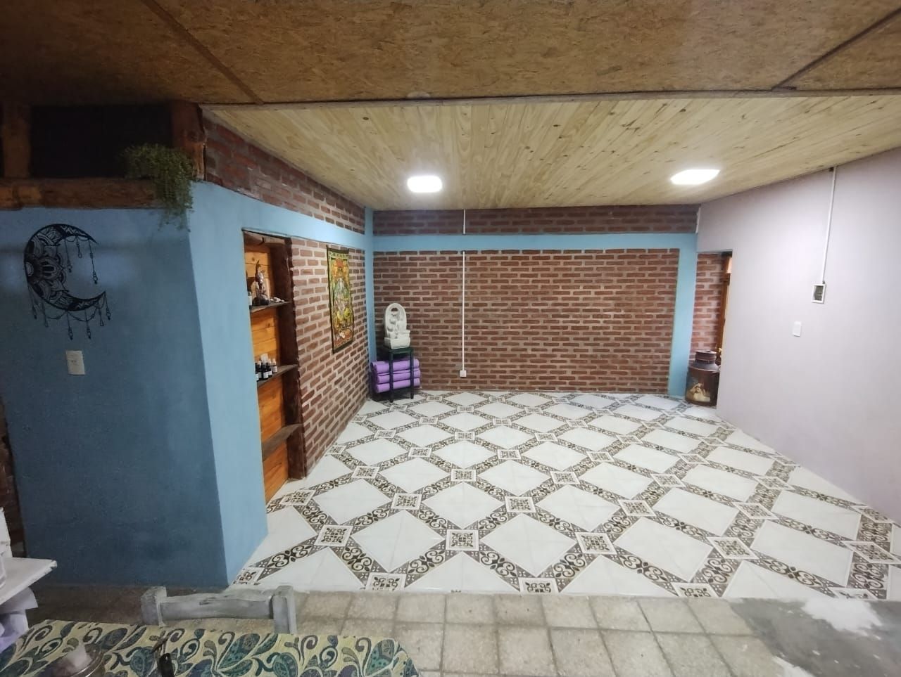 Habitación con paredes de ladrillo, techo de madera, suelo de baldosas, un cuadro, un estante y una estatua.