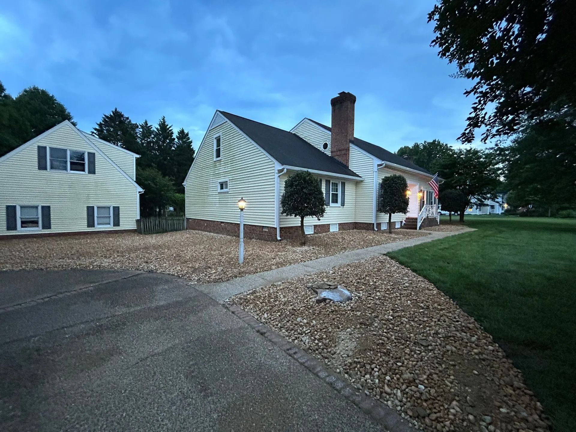 A cream-colored cottage-style house with a chimney and gravel yard under a twilight blue sky.