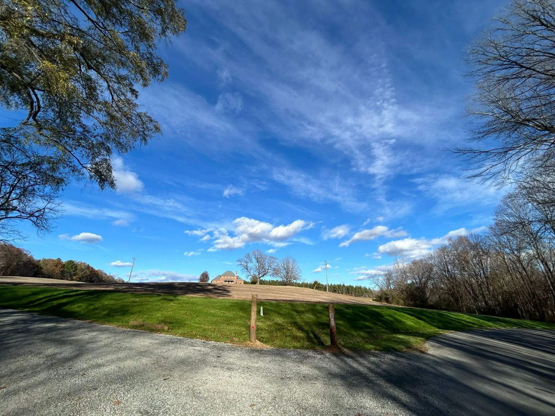 A gravel path leads to a grassy hill under a bright blue, cloudy sky, framed by trees on both sides.