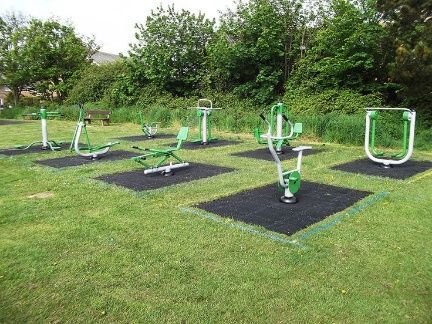 Una fila de equipos de ejercicio verdes y blancos en un parque.