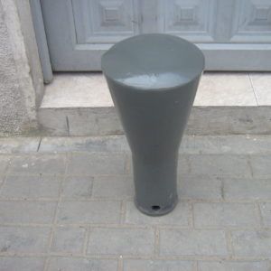 Un objeto gris en forma de cono está sentado sobre una acera de ladrillos frente a una puerta.