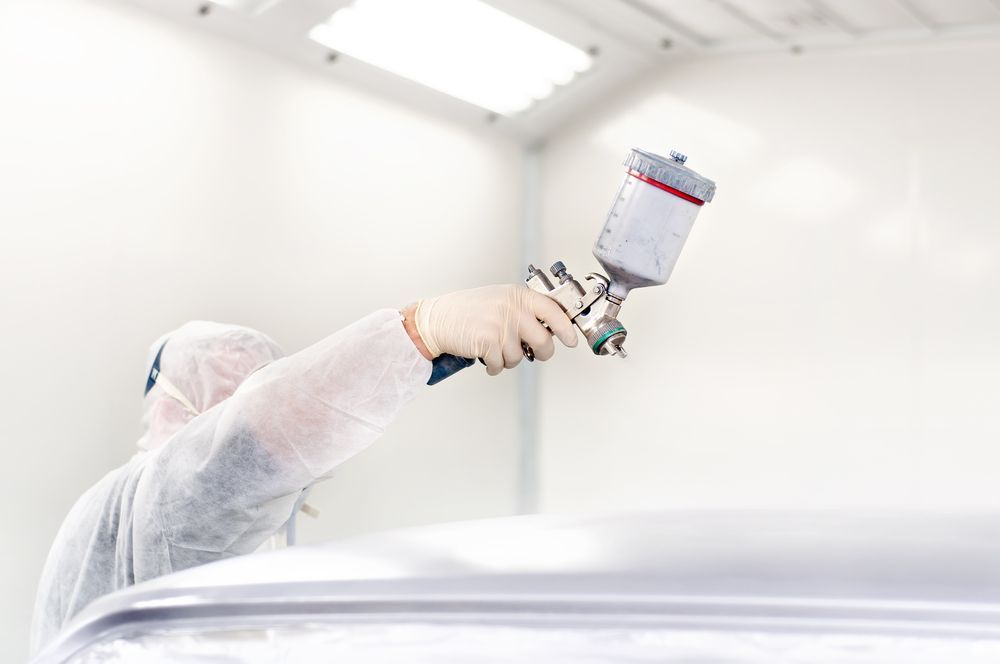 A Man Is Painting A Car In A Paint Booth — PK Crash Repairs In Ciccone, NT