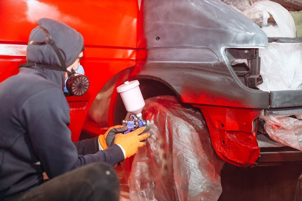 A Man Is Spray Painting A Red Car In A Garage — PK Crash Repairs In Uluru, NT