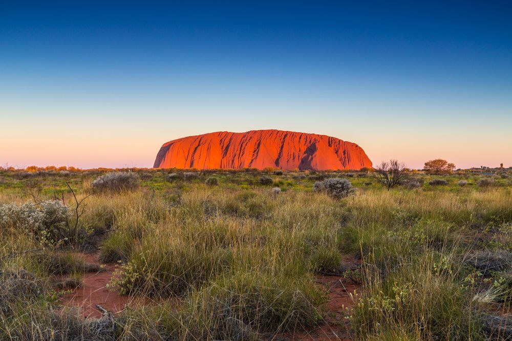 A Large Rock Formation In The Middle Of A Grassy Field — PK Crash Repairs In Uluru, NT