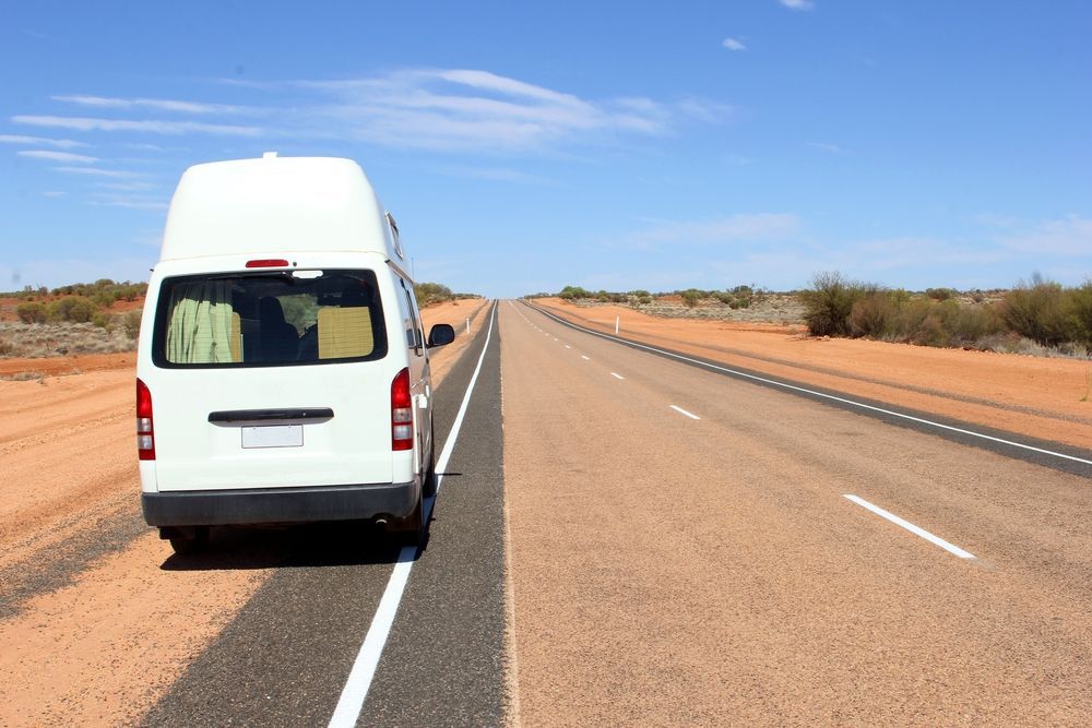 A White Van Is Driving Down A Dirt Road — PK Crash Repairs In Uluru, NT