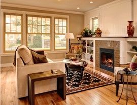 Living room with fireplace, windows, tan walls, hardwood floor, sofa, rug, and side tables.