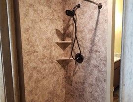 Corner shower with brown textured walls, black shower head, and two built-in triangular shelves.