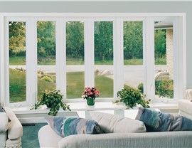 Large window with white frames overlooking a green yard and trees. A sofa with pillows is in the foreground.