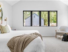 Bedroom with bed, neutral colors, large window overlooking a building and trees, and an armchair.