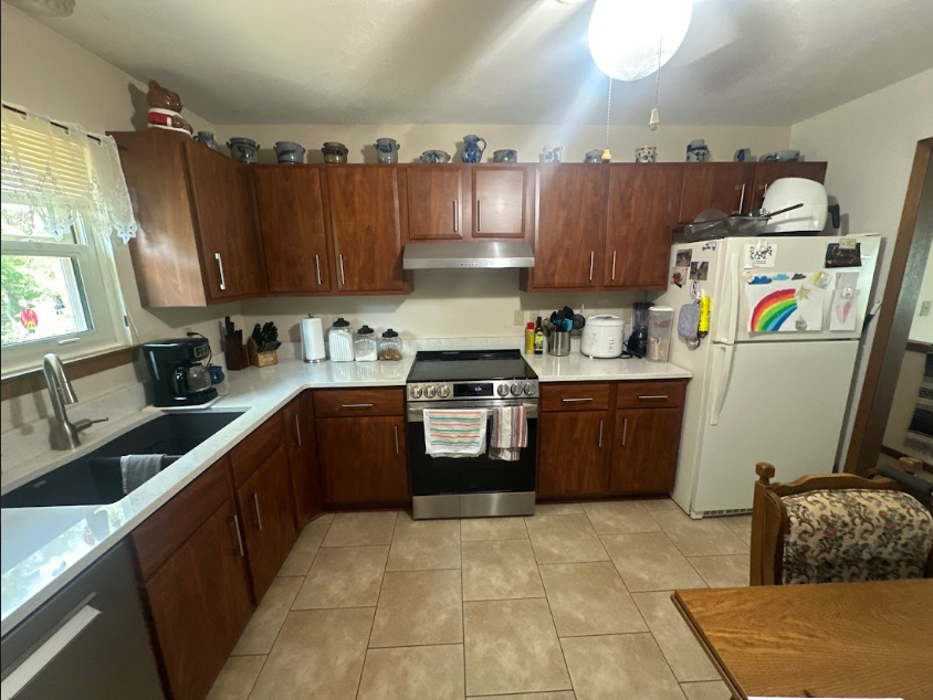 Kitchen with dark wood cabinets, white countertops, stainless steel appliances, and beige tile floor.