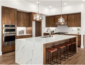 Modern kitchen with wood cabinets, white marble island, and pendant lights.