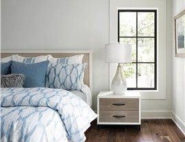 Bedroom with bed, blue bedding, nightstand, lamp, and window.