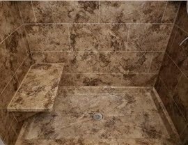 Shower stall with brown marble-like tiles, a built-in seat, and a drain.