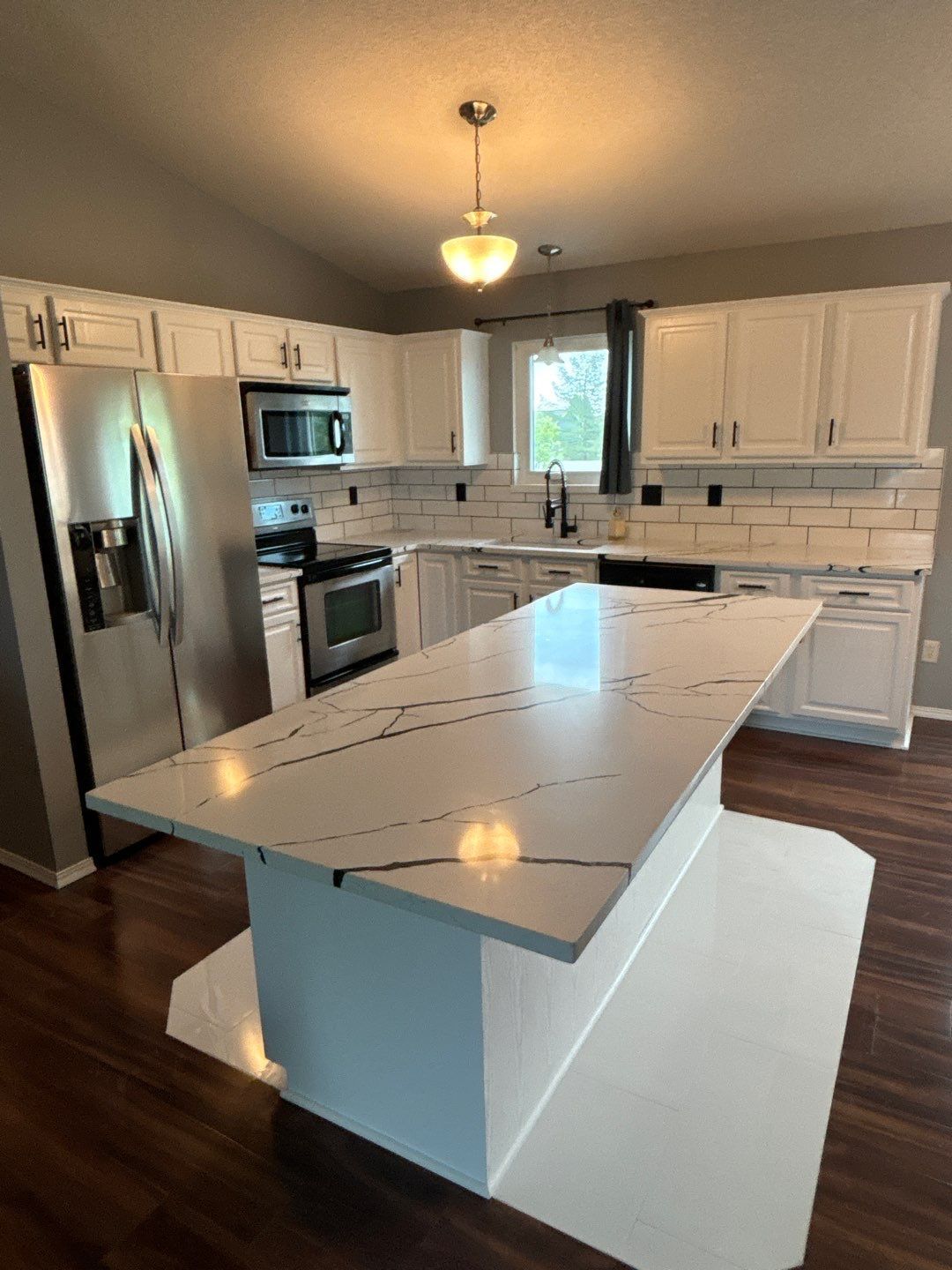 Modern white kitchen with quartz countertops and stainless steel appliances.