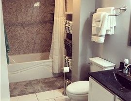 Bathroom with a bathtub, toilet, towels, and shelving. Gray walls with a white bathtub and toilet.