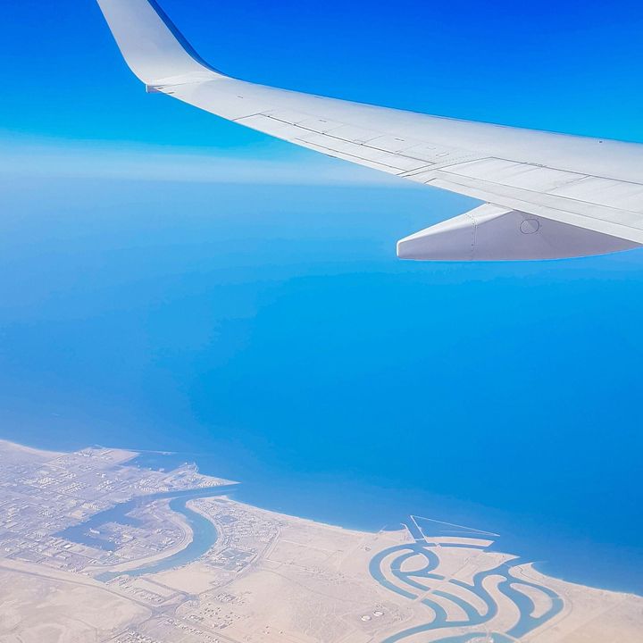 The wing of an airplane is flying over a body of water.