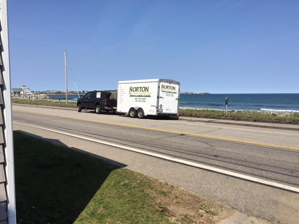 Black truck towing a white trailer on a coastal road, blue sky and ocean in the background.