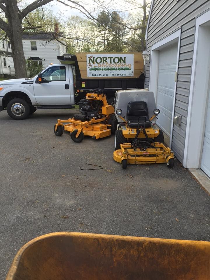 White truck and two yellow riding lawnmowers parked on asphalt next to a garage.