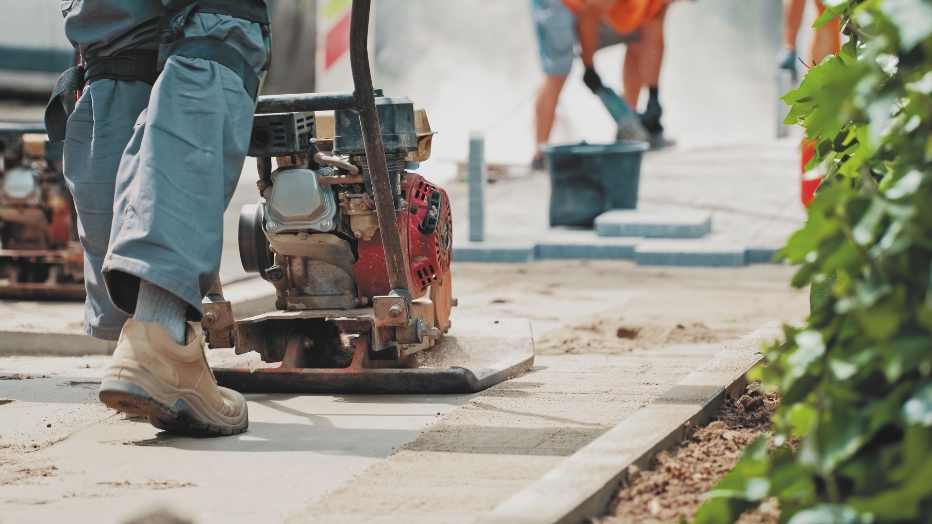 Local paving contractor using compactor machine to smooth new sidewalk surface outdoors.