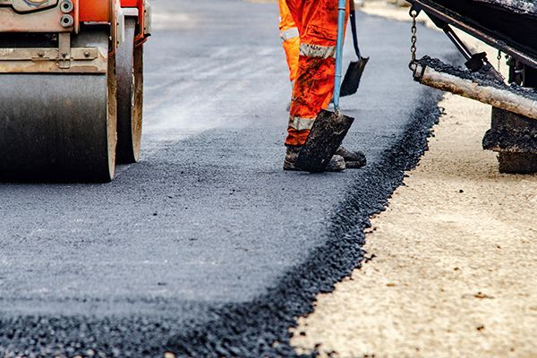 Local paving contractors in high-visibility gear are applying fresh hot asphalt to a road surface.