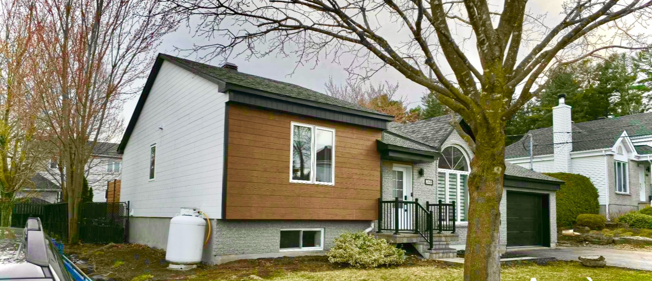 Une petite maison avec un garage et un arbre devant.