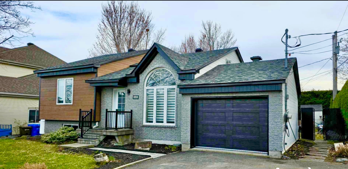 Une petite maison avec une porte de garage noire et un toit gris.