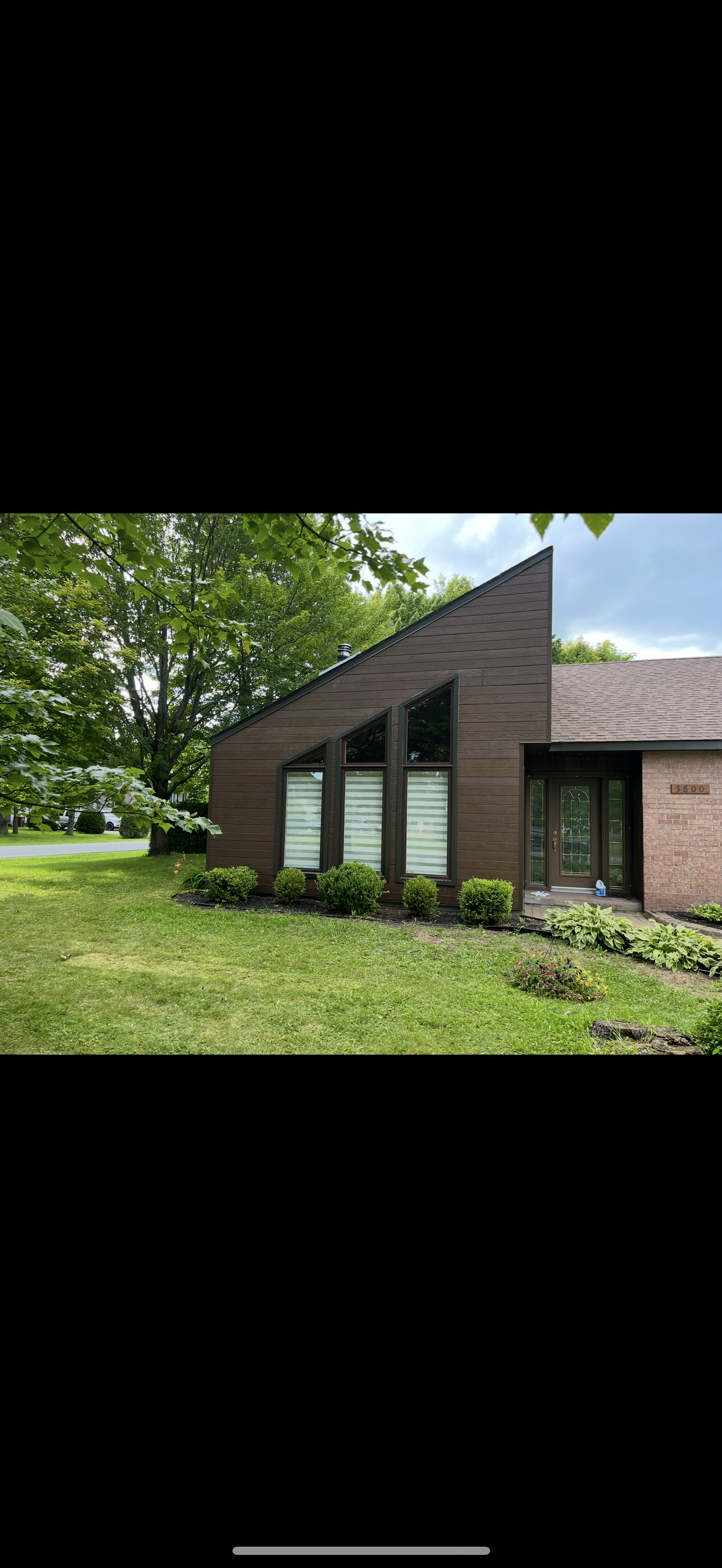 Une maison en briques avec un toit en pente est située au sommet d'un champ verdoyant.