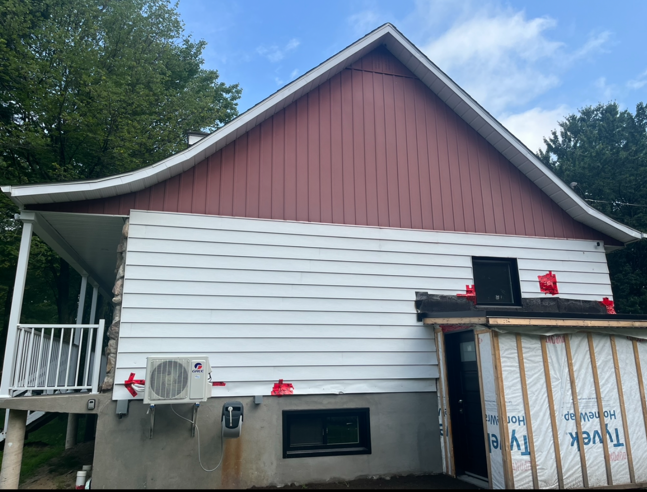 Une maison avec un toit rouge et un revêtement blanc est en cours de rénovation