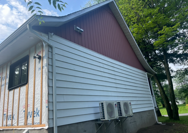 Une maison rouge avec un revêtement blanc et deux climatiseurs sur le côté.