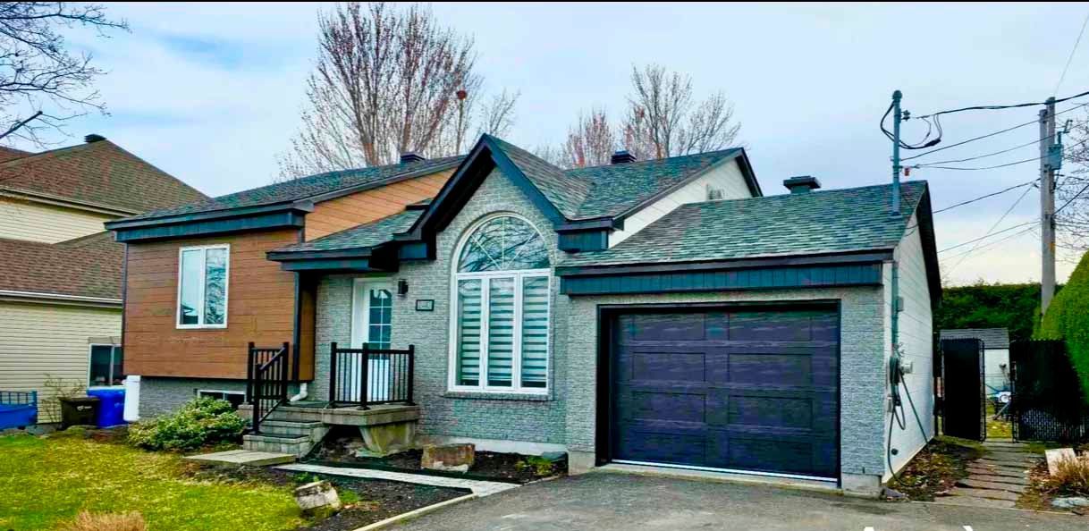 Une petite maison avec une porte de garage noire et un toit gris.