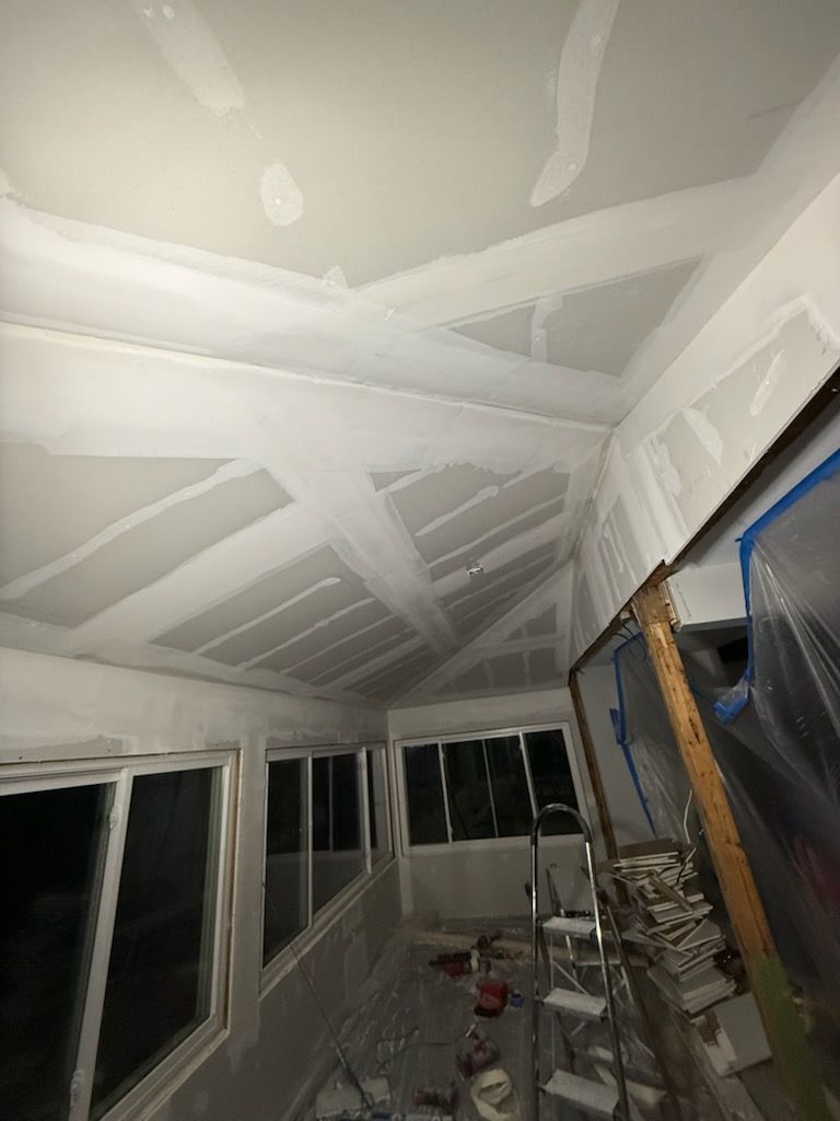 Interior view of room under construction with white drywall ceiling and walls, windows, and ladder.