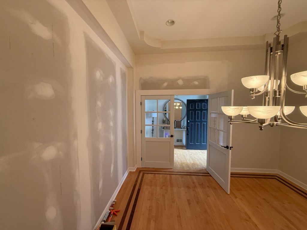 Empty dining room with hardwood floors, white walls, and a chandelier, leading into a blue-lit adjacent room.