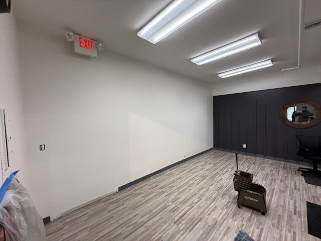 A bright room features a long white wall, a dark wood-paneled accent wall with a circular mirror, and light wood flooring.