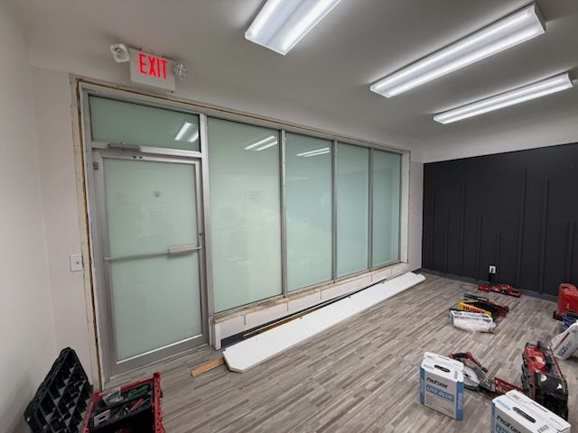 A bright, empty room with a glass-paned exit door, frosted windows, grey wood-look flooring, and construction tools.