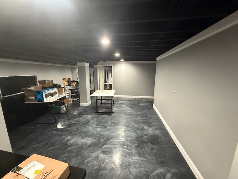 Basement room with black ceiling, gray walls, and epoxy floor. Unfinished storage area.