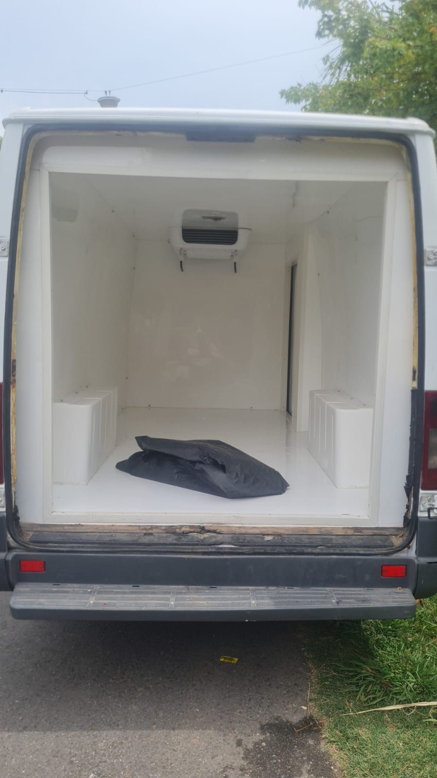 Furgoneta de carga blanca estacionada en una calle con un edificio al fondo.