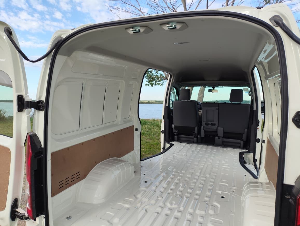 Vista interior de una camioneta de carga blanca con las puertas abiertas, revelando un área de carga vacía y asientos delanteros.
