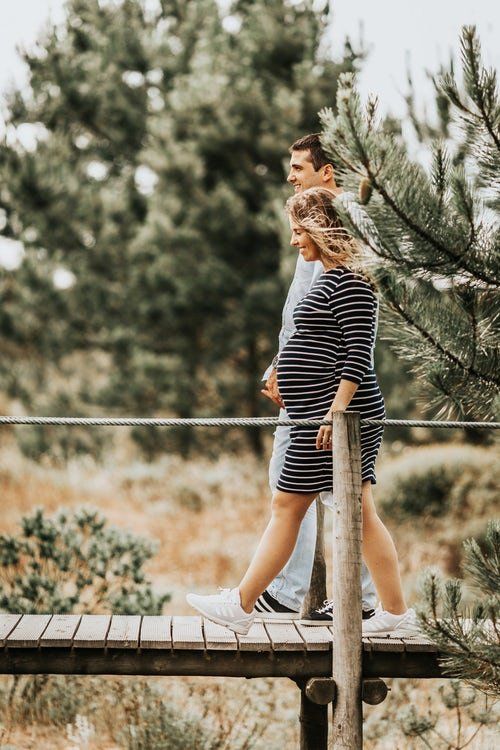 pregnant woman and man walking on wood bridge