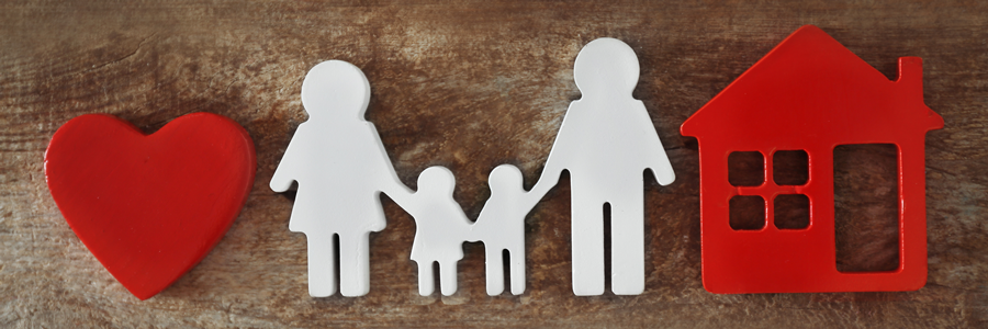 A family is standing next to a red heart and a red house.