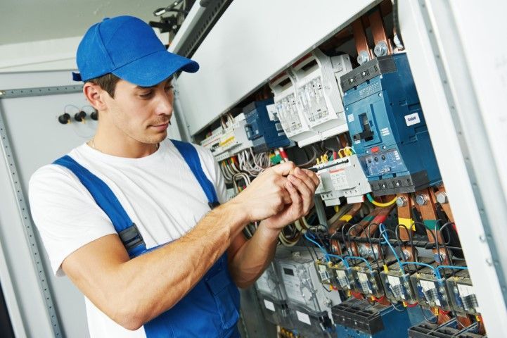 Technician in blue overalls adjusting wiring inside an electrical control panel