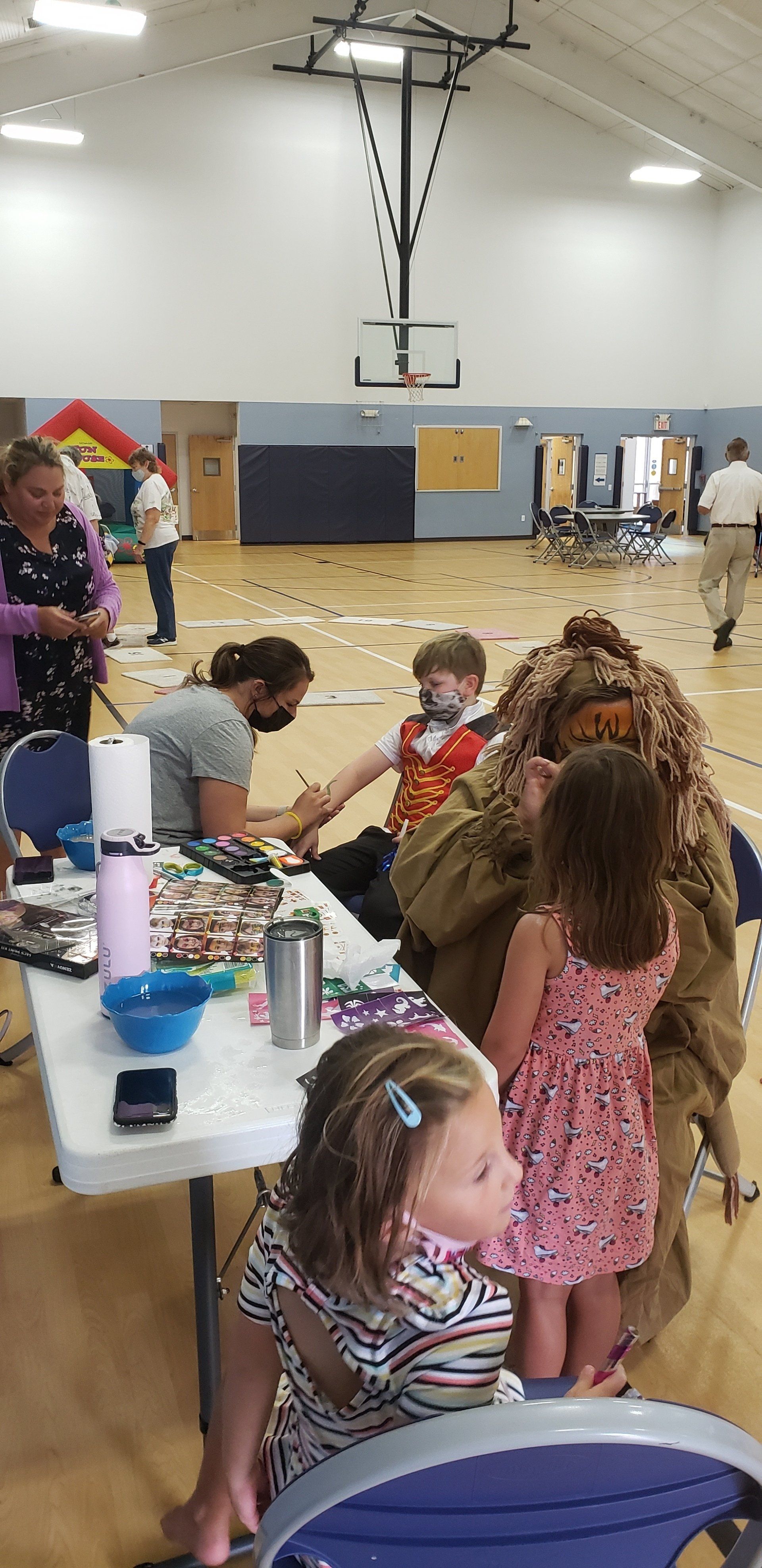 Children getting face paint at a community event in a gymnasium.