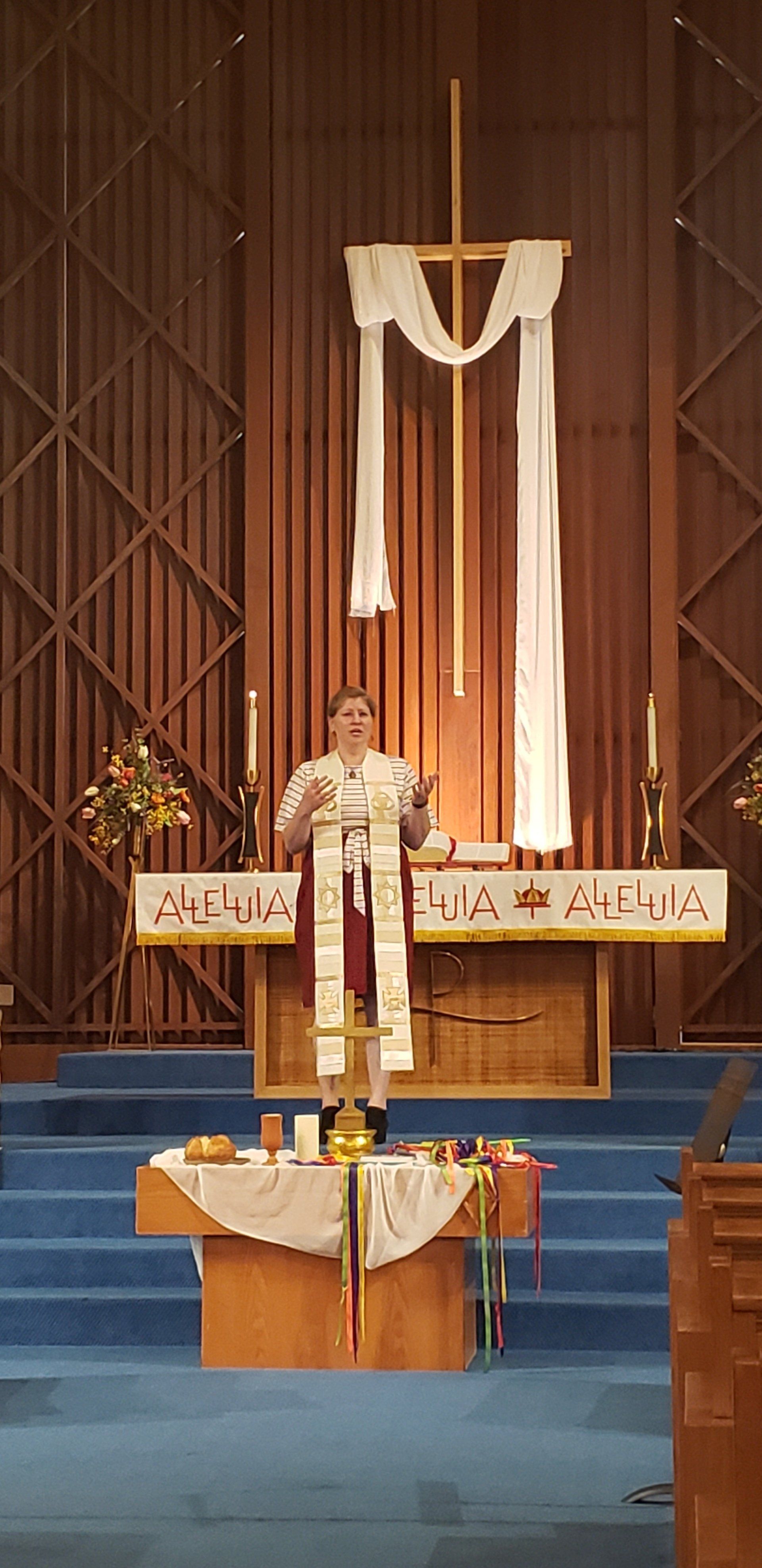 A person wearing a white robe stands on a blue carpet in front of a church altar.