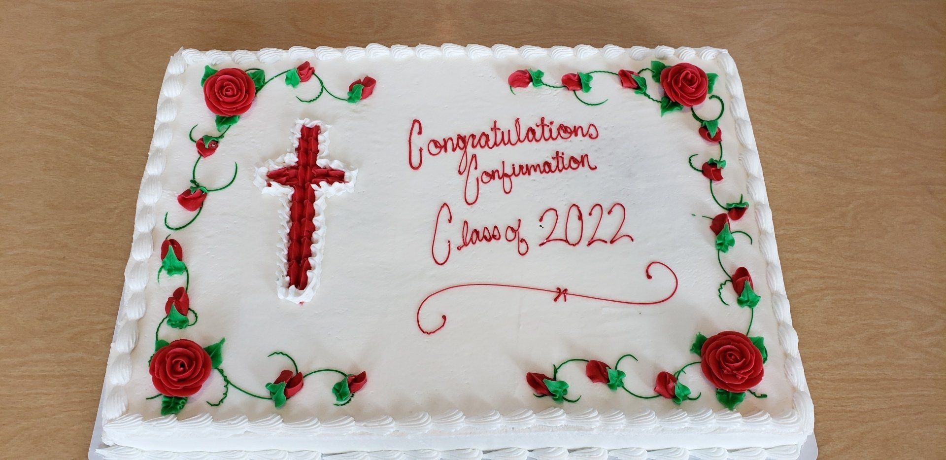 Cake decorated with a red cross, roses, vines, and text: 