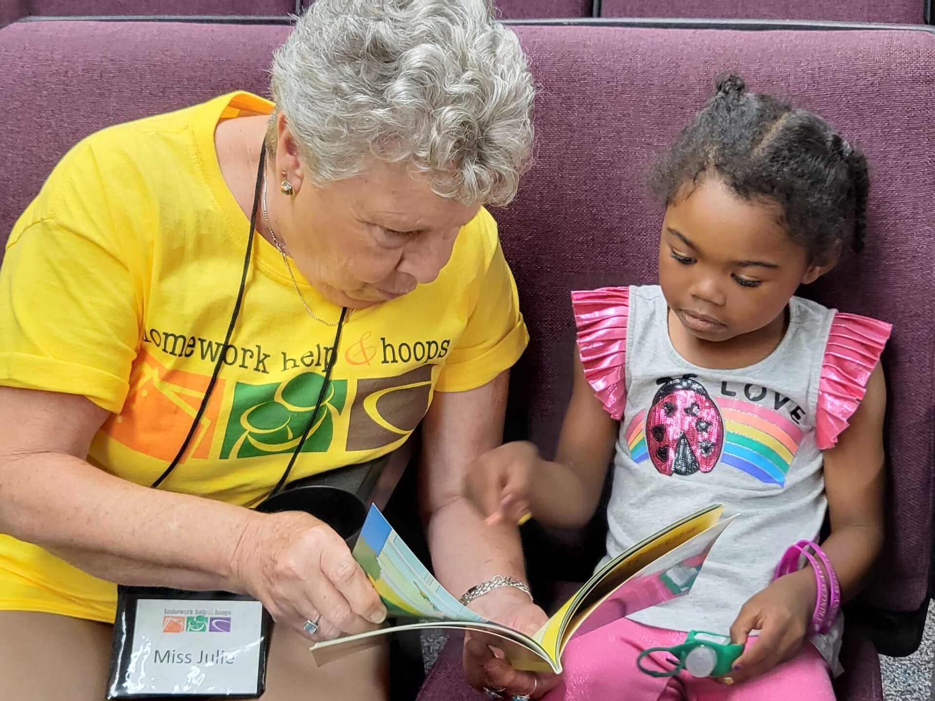 Woman in yellow shirt reading to a young girl. They sit together, looking at the book.