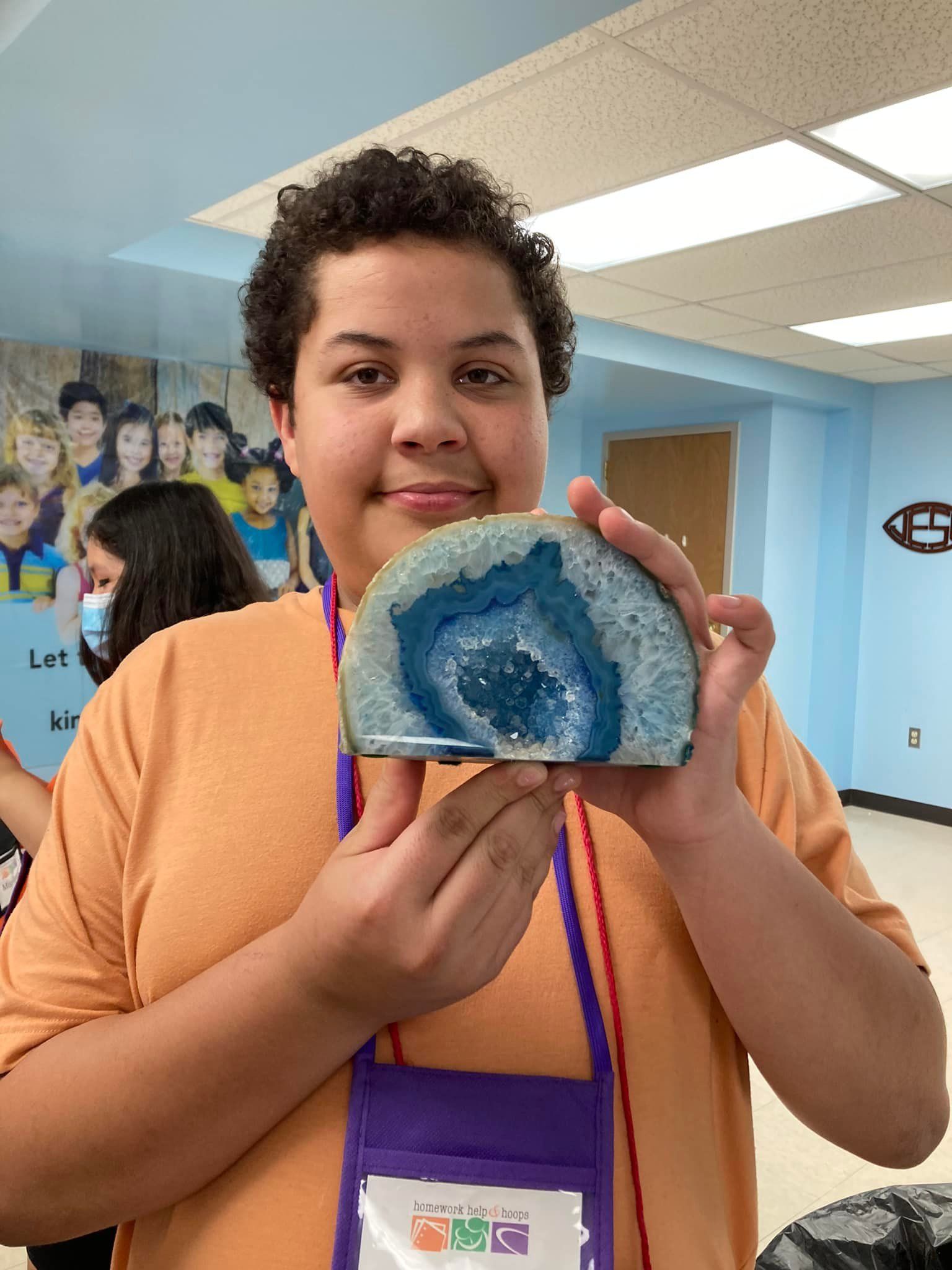 Young person holding a blue and white geode. They are in a room with other people.