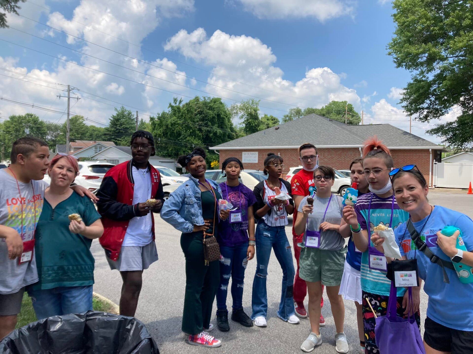 Group of people, diverse ages, eating popsicles outdoors on a sunny day; some smiling, some holding treats.