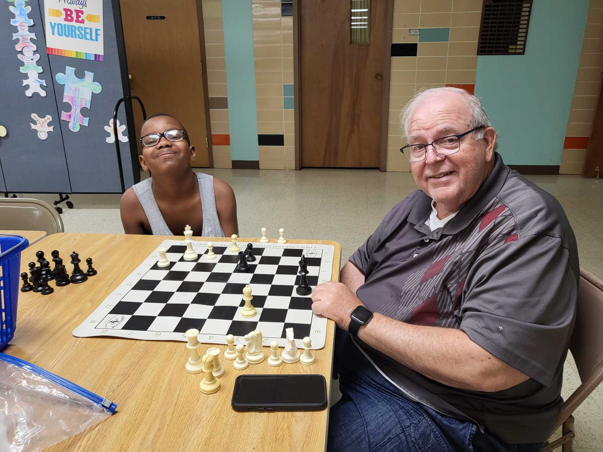 A young boy and an older man smiling while playing chess at a table indoors.