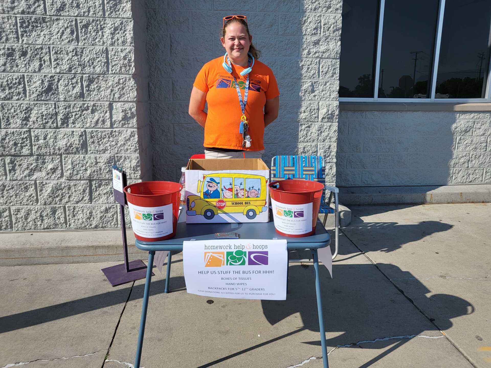 Woman at table with donation buckets outside brick building.
